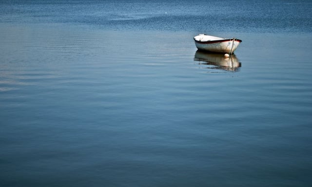 Stock photo of rowboat on calm and peaceful lake.