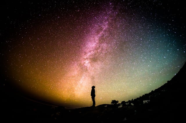Photo of person standing at night with background of Milky Way Galaxy.