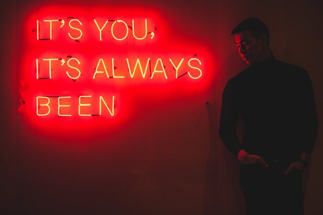 Man on stage with neon sign behind him.