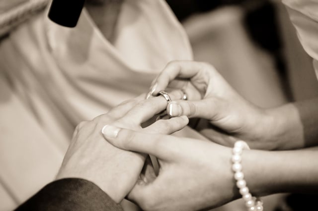 Stock photo of bride placing wedding ring on groom's finger.